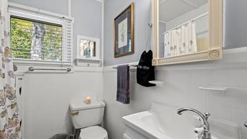 A bathroom with a toilet, sink, mirror, and window with blinds.