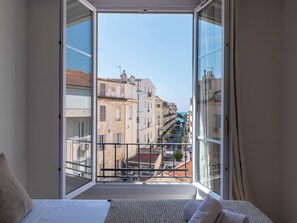 Ein Zimmer mit großem Fenster, einem Bett und Blick auf die Stadt.