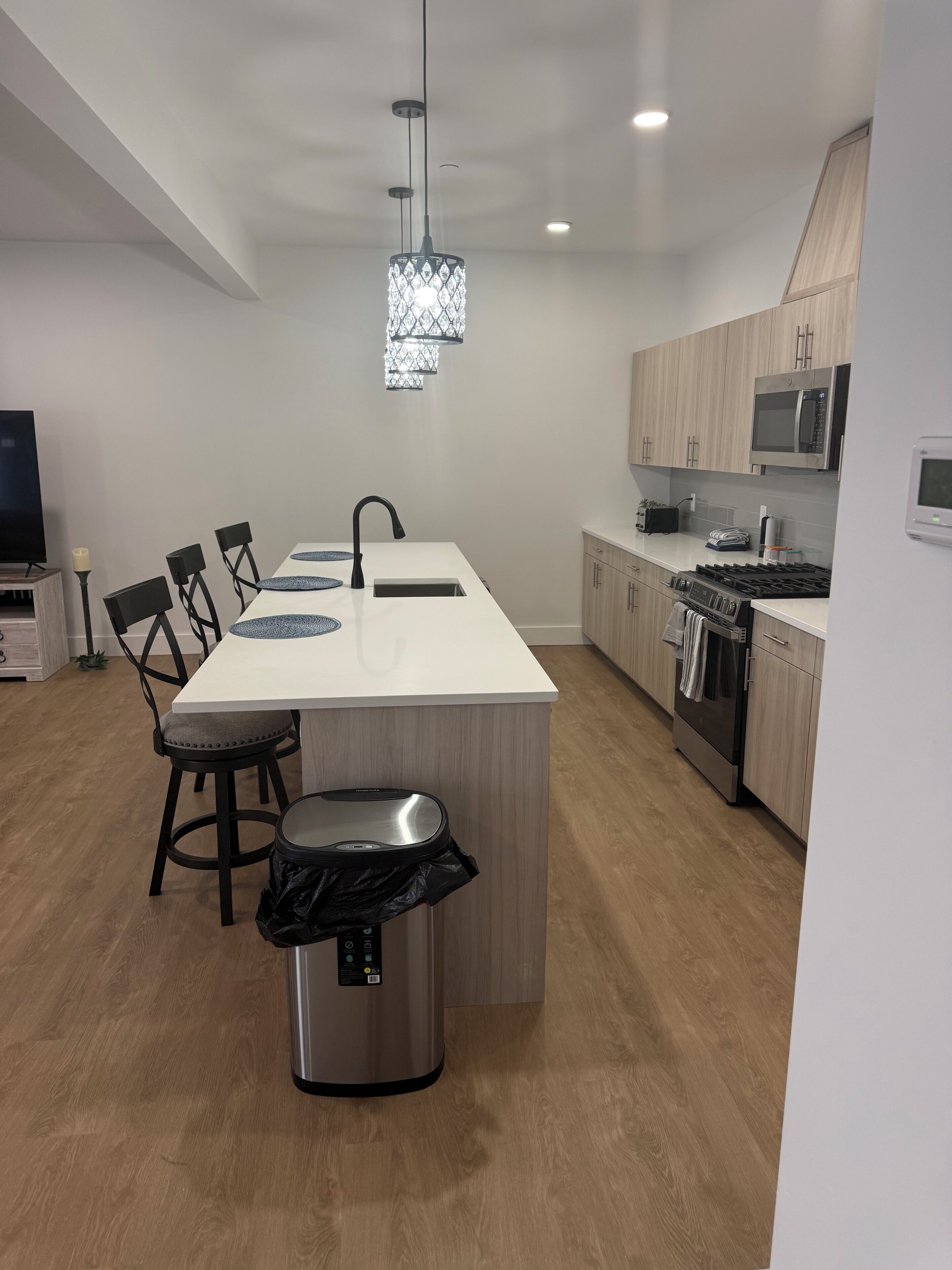 Une cuisine moderne dotée d’un îlot central, d’appareils électroménagers en acier inoxydable et d’un luminaire suspendu.