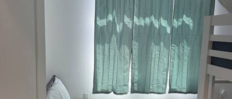 A room with a bed, a window with curtains, a ceiling fan, and a door.
