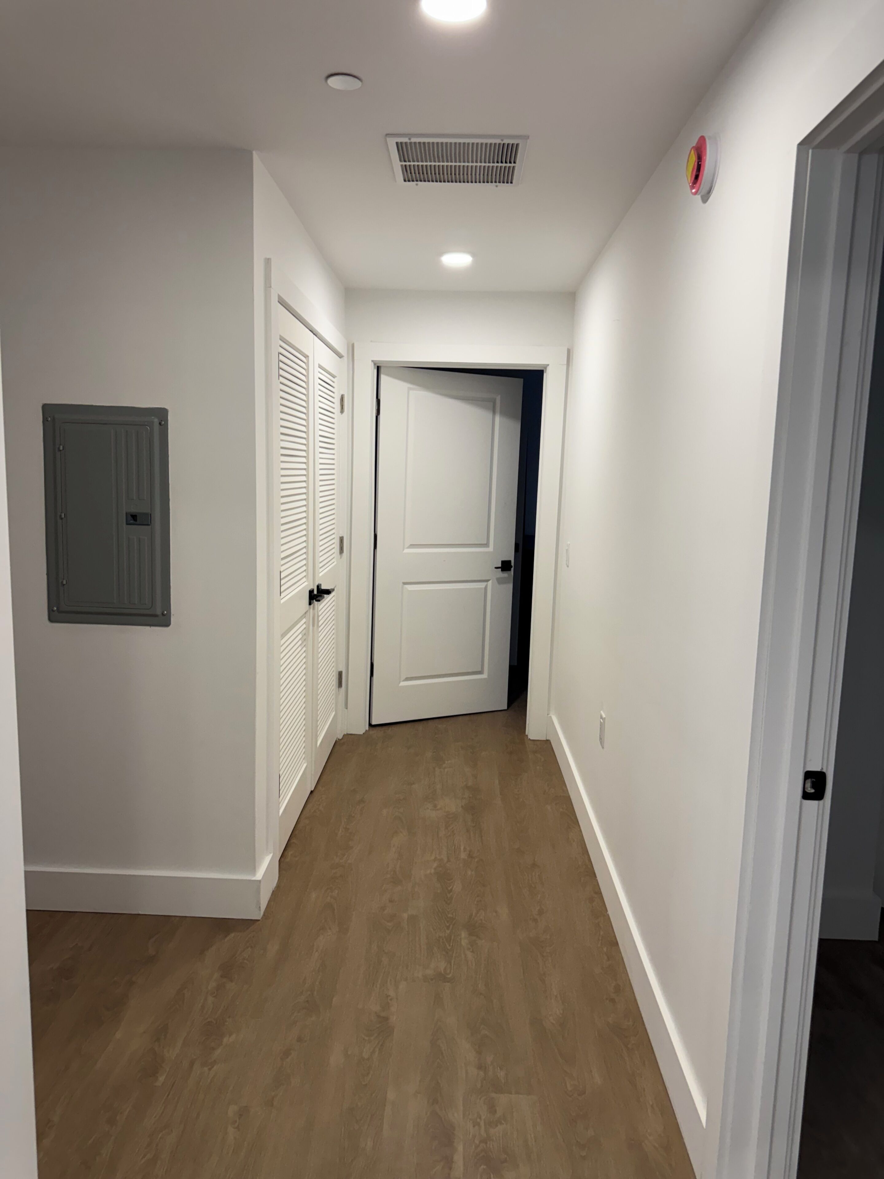 A hallway with white walls, a wooden floor, and a door at the end.