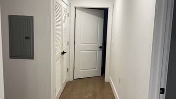 A hallway with white walls, a wooden floor, and a door at the end.