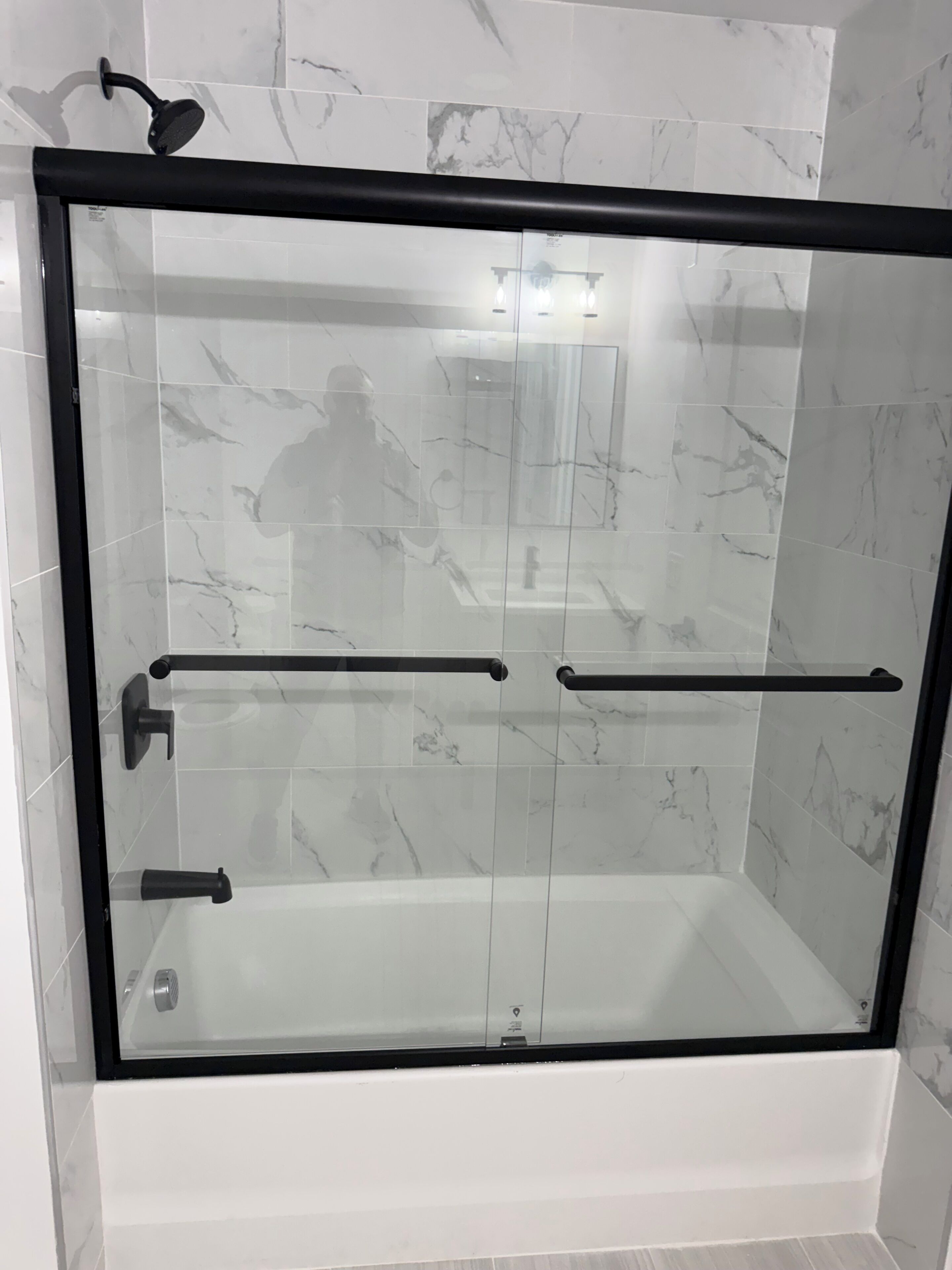Ducha con paredes de cristal, marco negro, azulejos con diseño de mármol y pasamanos.