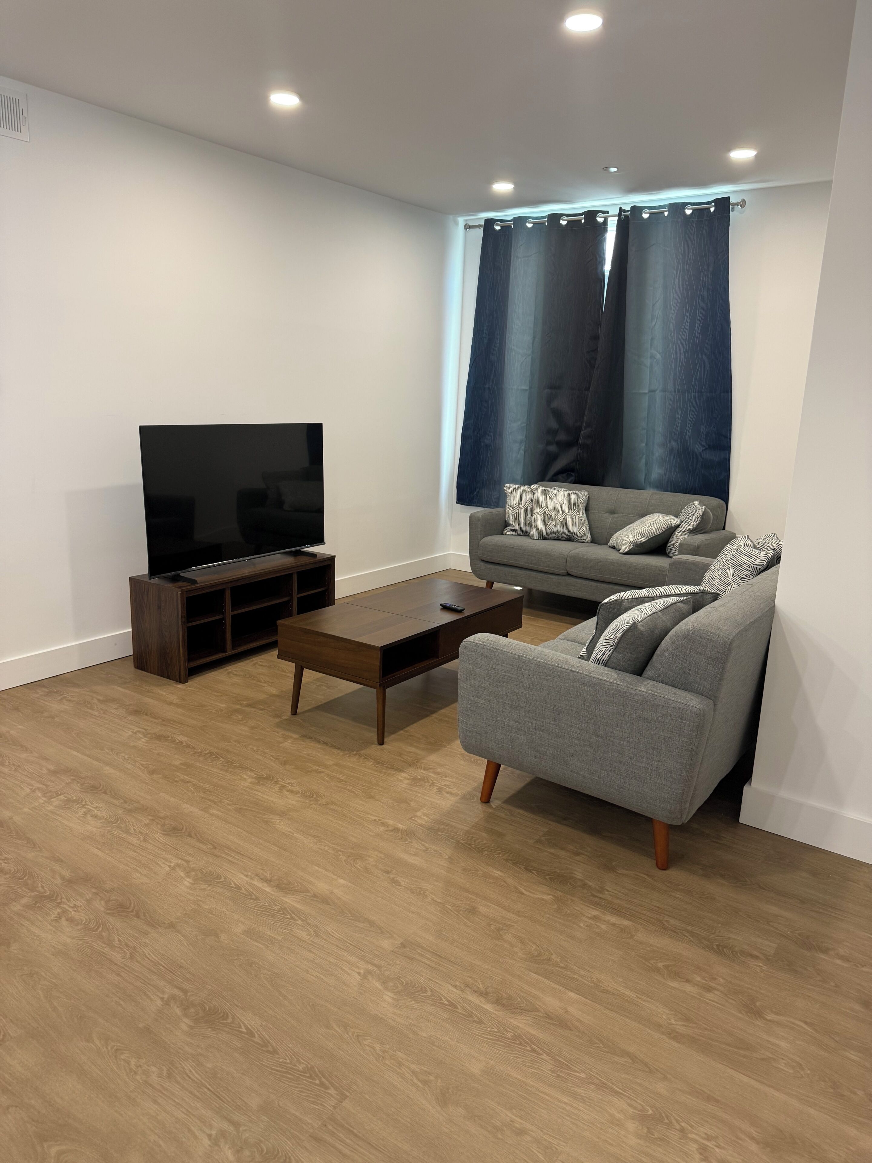 A modern living room with a flat-screen TV, a grey sofa, and a wooden coffee table.