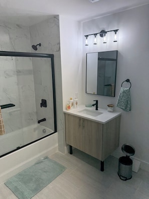 A modern bathroom with a glass shower enclosure, a white sink, a mirror, and a light fixture above the mirror. - Coral Sands (Seaside Heights)