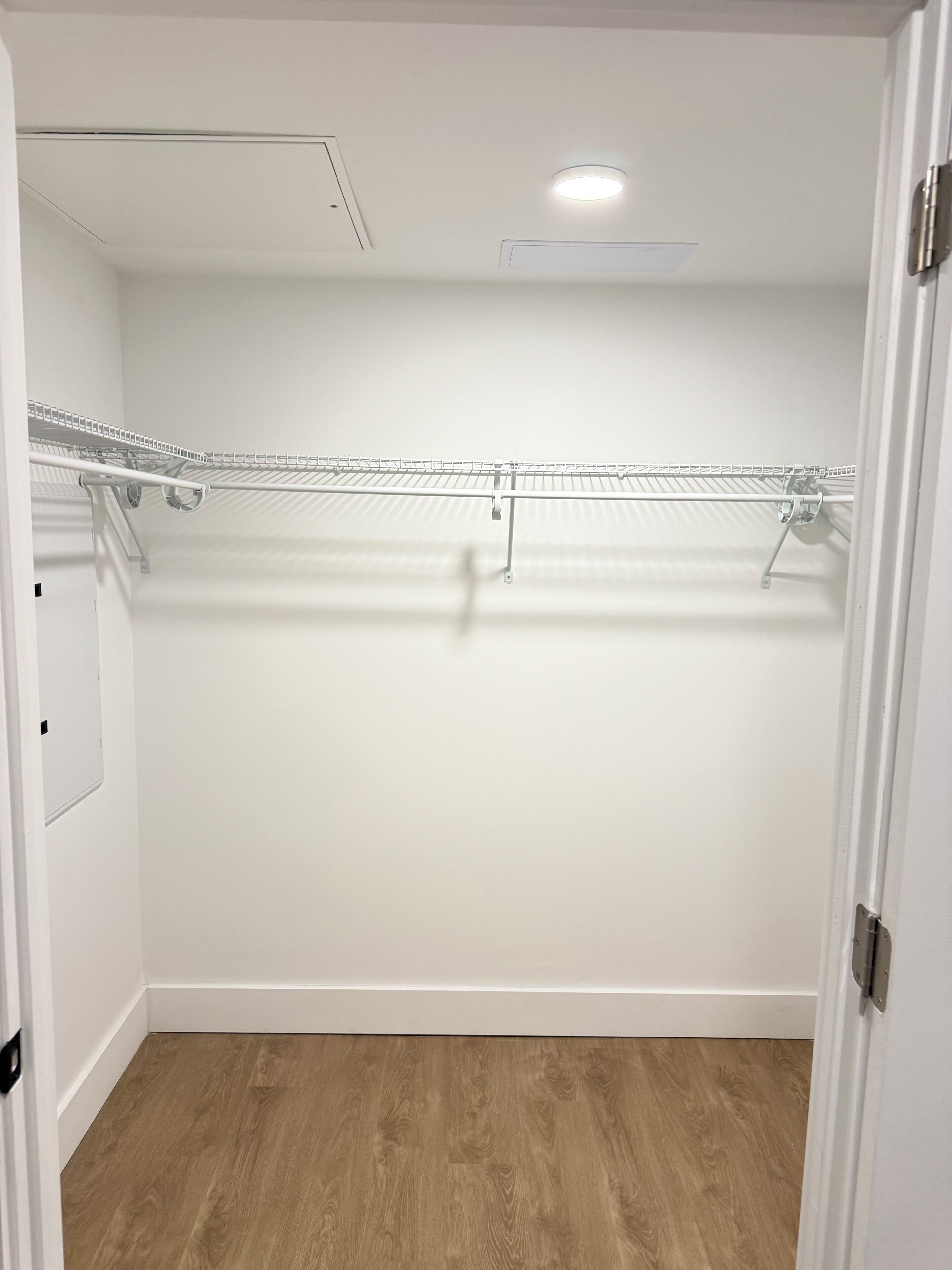 A walk-in closet with a wooden floor, white walls, and a metal shelving unit.