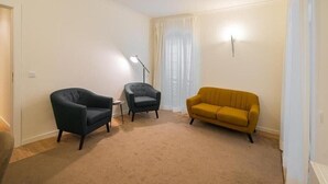A room with a beige carpet, two armchairs, a sofa, a floor lamp, and a window with sheer curtains. - Residencial Farol (Ilhavo)