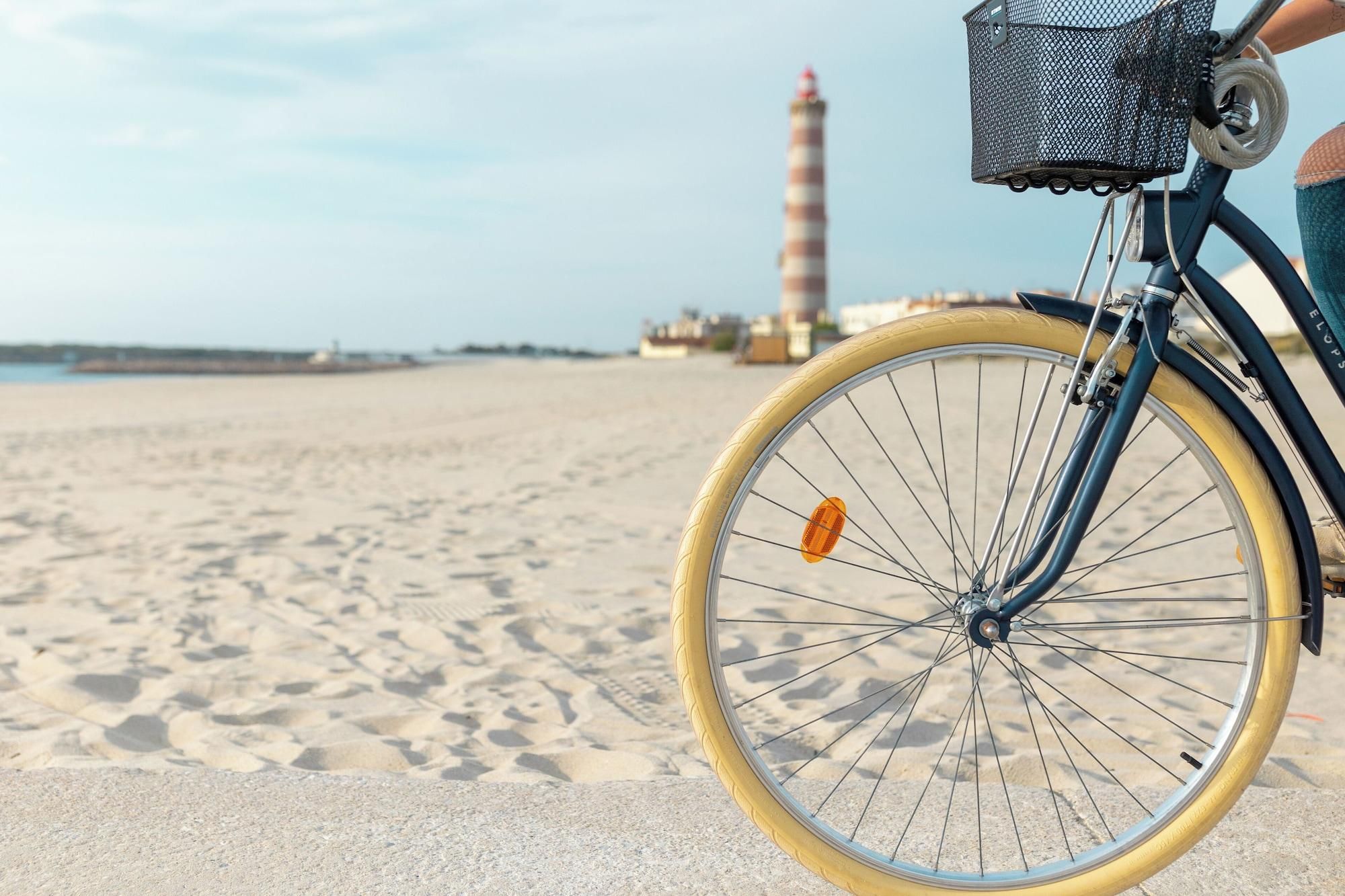 A bicycle with a basket and a yellow tire on a sandy beach with a lighthouse in the background.