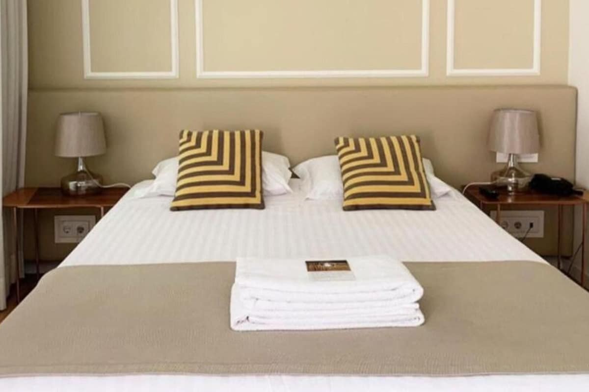 A neatly made bed with striped pillows, a folded towel, and a bedside table with a lamp and a phone.