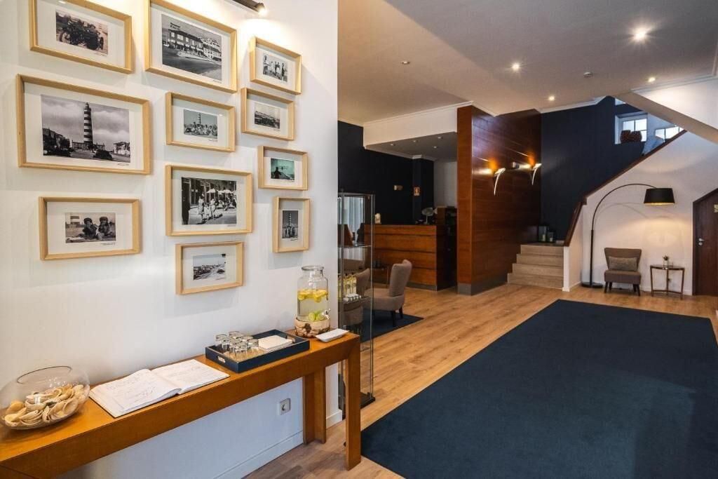 Een hotellobby met ingelijste foto's aan de muur, een receptiebalie en een trap.