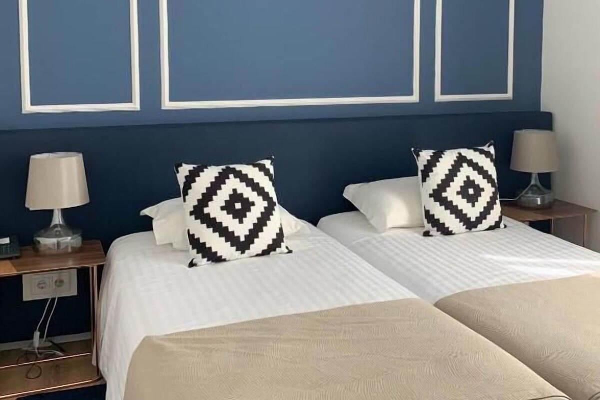 A hotel room with a double bed, two bedside tables with lamps, and a blue accent wall.