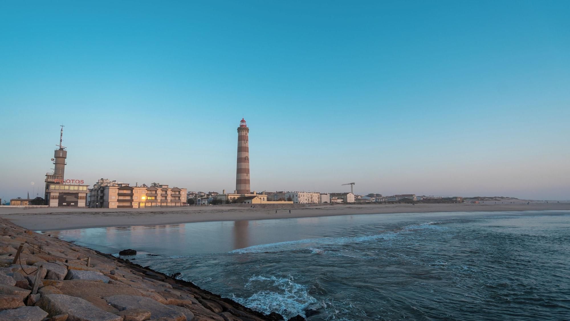 Paisaje costero con un faro, edificios y una playa.