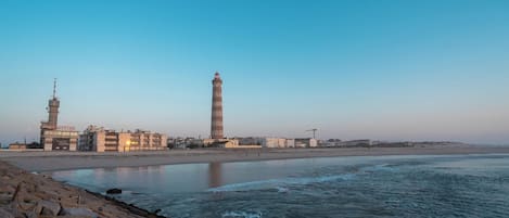 A coastal scene with a lighthouse, buildings, and a beach.