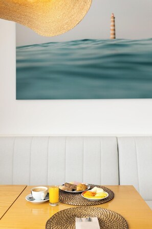 A dining area with a table set for breakfast, a painting of a lighthouse, and a woven placemat.