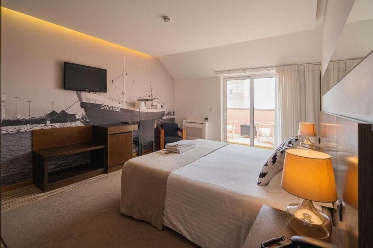 A hotel room with a bed, desk, chair, television, and a large window.