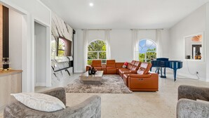 A spacious living room with a sectional sofa, a piano, and a large window offering a view of greenery.