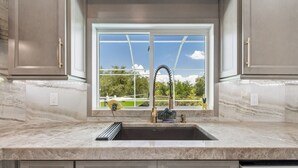 A kitchen with a marble countertop, a window with a view of greenery, and a sink with a faucet.