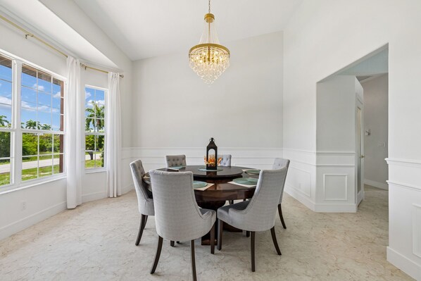 Une salle à manger avec une table ronde, six chaises, un lustre et de grandes fenêtres avec des rideaux.