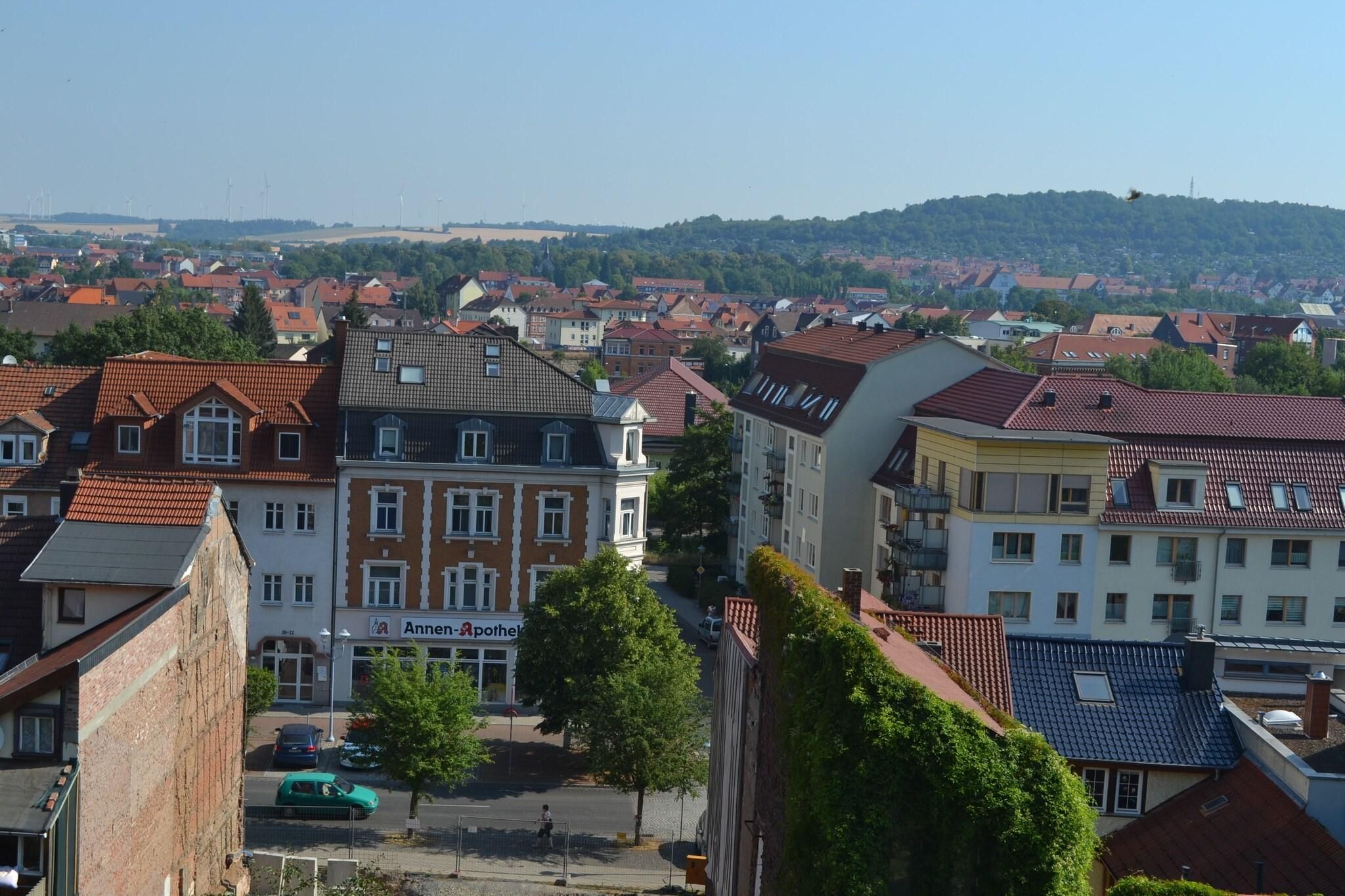 Ein Wohngebiet mit einer Mischung aus traditionellen und modernen Gebäuden, einer Apotheke im Blickfang und einer hügeligen Landschaft im Hintergrund.