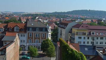 Ein Wohngebiet mit einer Mischung aus traditionellen und modernen Gebäuden, einer Apotheke im Blickfang und einer hügeligen Landschaft im Hintergrund.