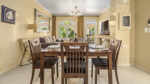 A dining area with a wooden table and chairs, a sofa, a TV, and a chandelier. - Tropical Getaway w/ Pool & Patio @ Wacamaya Condos (Noord)