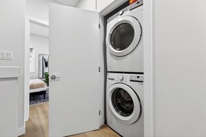 A laundry room with two front-loading washing machines, a door to a bedroom, and a small rug on the floor. - The Executive Escape|Spacious 3BR Near Downtown|Free parking|Free WiFi|Pooltable (Edmonton)