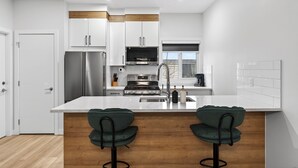 Una cocina moderna con armarios blancos, electrodomésticos de acero inoxidable, una isla central con taburetes y piso de madera.