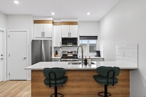 A modern kitchen with white cabinets, stainless steel appliances, a central island with bar stools, and a wooden floor. - The Executive Escape|Spacious 3BR Near Downtown|Free parking|Free WiFi|Pooltable (Edmonton)