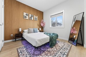 A bedroom with a wooden wall, a bed with white bedding, a patterned rug, a window with a view, and a mirror. - The Executive Escape|Spacious 3BR Near Downtown|Free parking|Free WiFi|Pooltable (Edmonton)