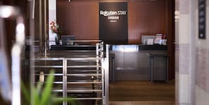 A reception area with a wooden reception desk, a vase with flowers, and a wall with the text 'Rakuten Stay URBAN Ogikubo'. - Rakuten STAY URBAN ogikubo (Tokyo)