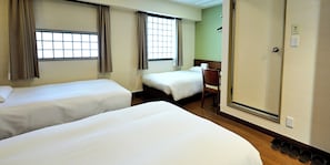Ein Hotelzimmer mit zwei Betten, Holzboden, einem Sessel und einem Spiegel.
