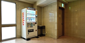 Ein Automat mit der Aufschrift 'DyDo' in einer Diele mit gefliesten Wänden und einer Tür.