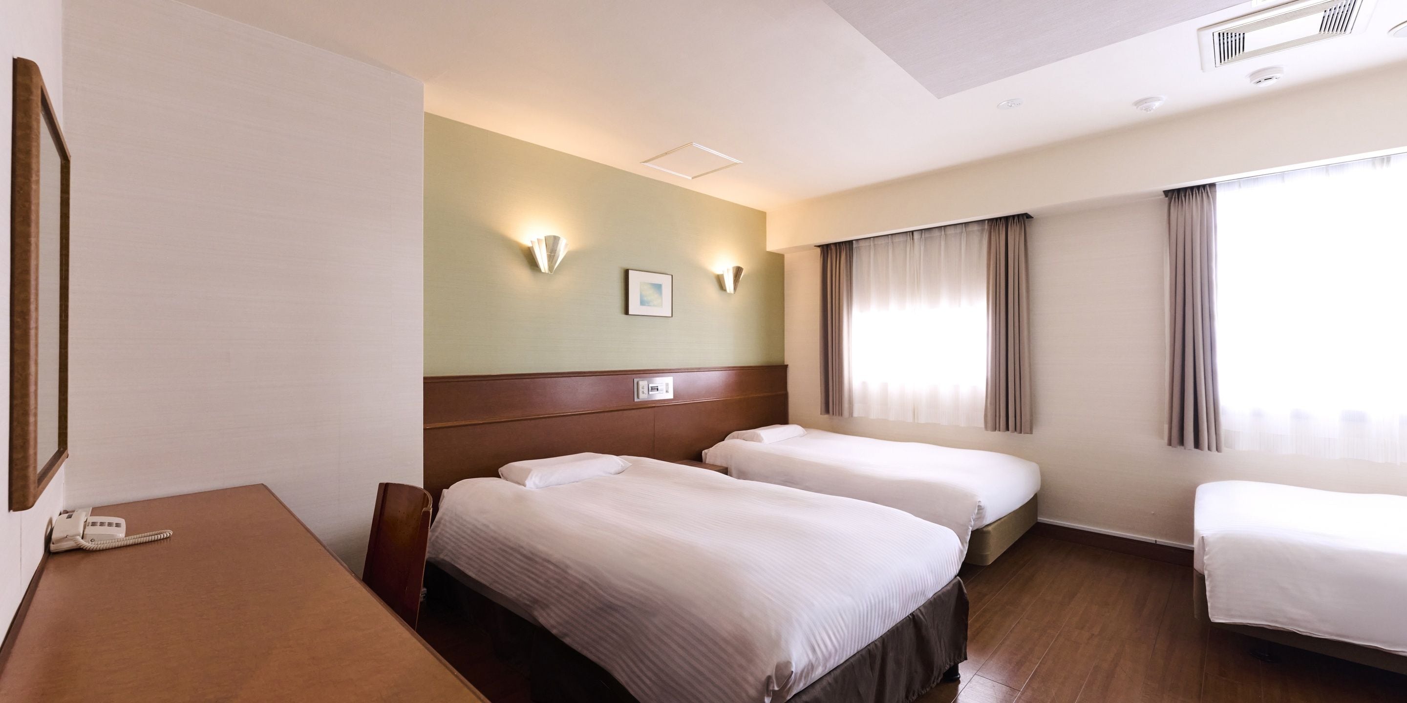 A hotel room with two beds, a desk, a telephone, and a wall-mounted light fixture.