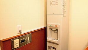 Un distributeur de glaçons fixé au mur, doté d’une horloge numérique, d’une prise de courant et d’un bouton-poussoir.