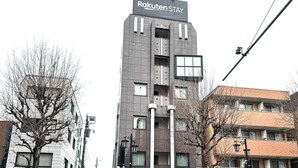Un bâtiment moderne, sur lequel on peut lire l’inscription « Rakuten Stay », se distingue par sa structure à plusieurs étages, ses balcons et sa façade plate.