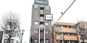 Ein modernes Gebäude mit einem Schild, auf dem 'Rakuten Stay' steht, mit einer mehrstöckigen Struktur, Balkonen und einer glatten Fassade.
