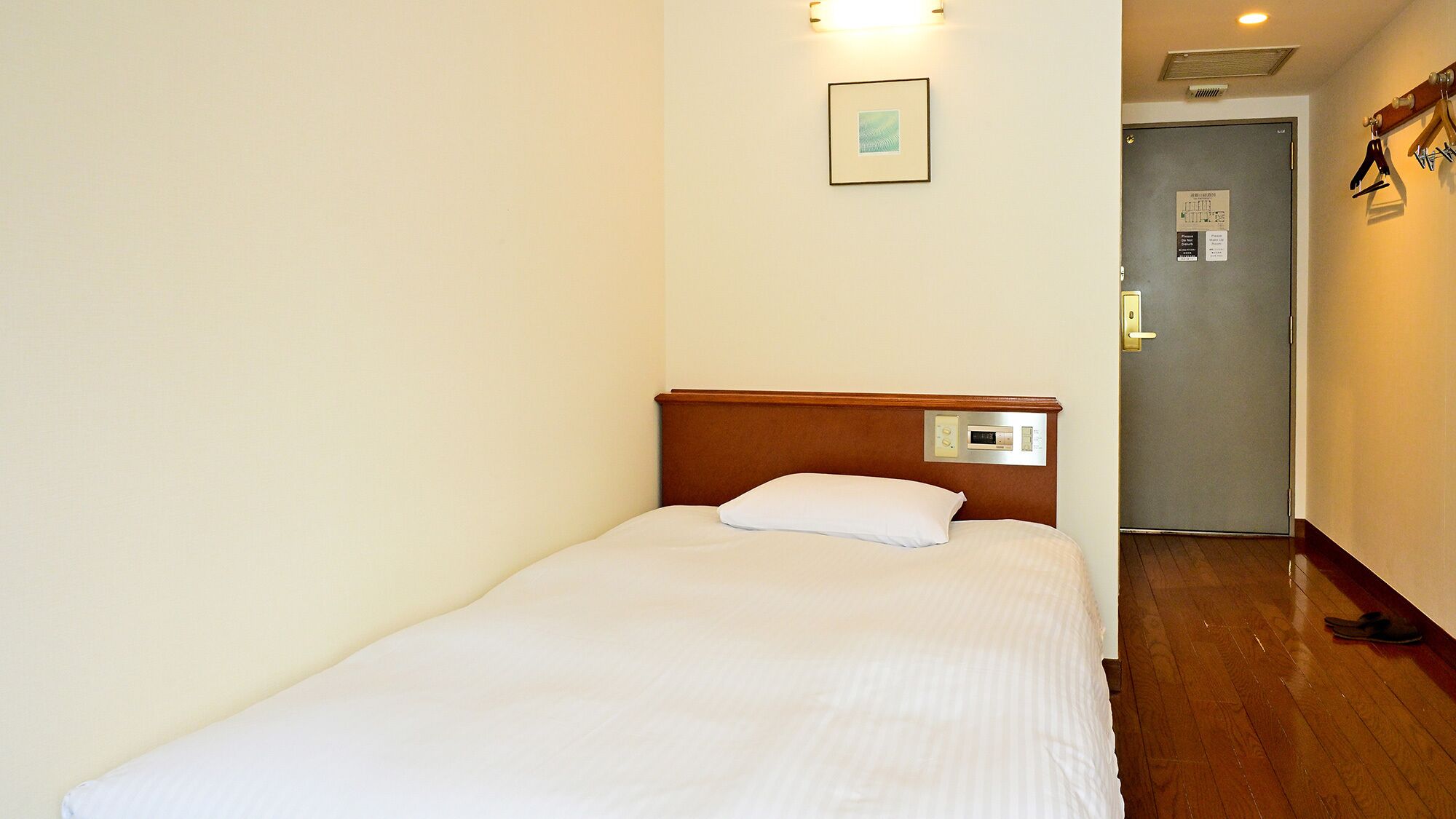 A single bed with a wooden headboard, a control panel, and a framed picture on the wall.