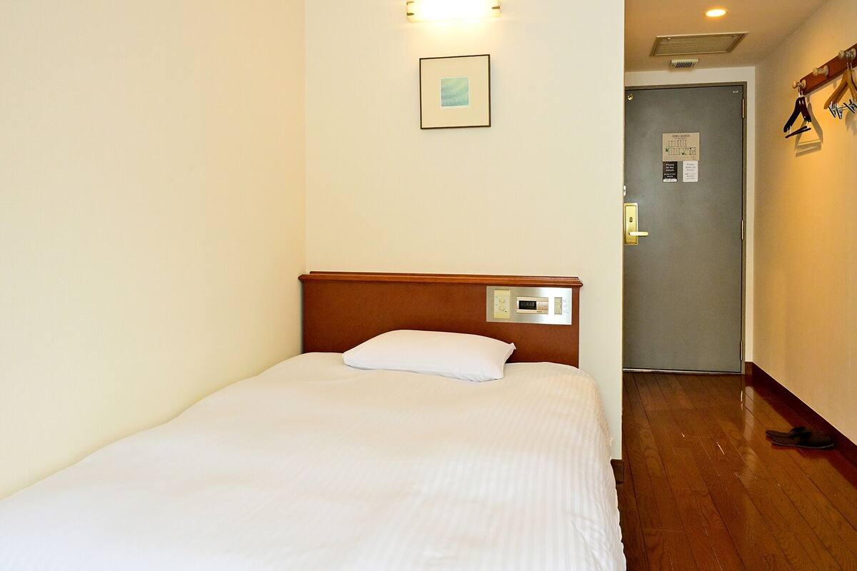 Una cama individual con cabecera de madera, panel de control y un cuadro en la pared.