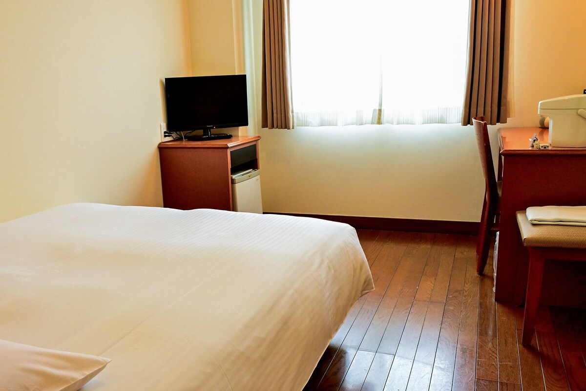 A hotel room with a bed, a desk, a television, and a window with curtains.