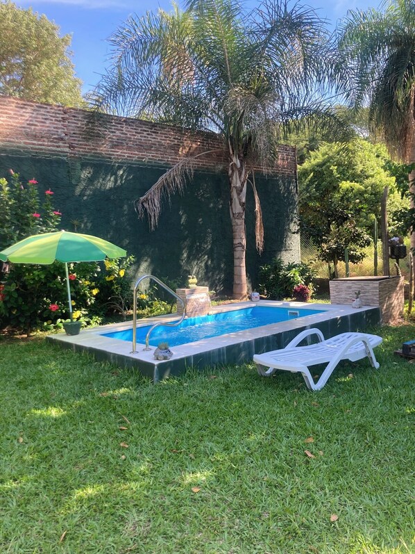 A swimming pool with a ladder, a lounge chair, and a green umbrella.