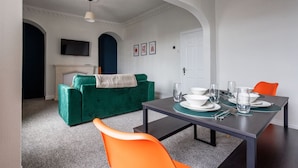 A dining area with a table set for four, a green sofa, and a television mounted on the wall. - Sunderland City Stay Secure Parking Sleeps 4 (Sunderland)