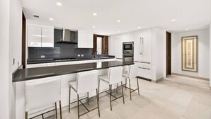 A modern kitchen with a black countertop, white cabinets, and a bar area with white chairs. - New Family Luxury Golf Penthouse With Private Pool (Punta de Mita)