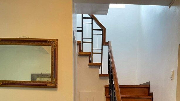A living room with a staircase, a framed mirror, a coffee table with flowers, and two sofas.