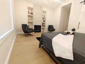 A modern bedroom with a bed, two chairs, a fireplace, and built-in shelves. - Luxury Home With Three Bedrooms and Living Room (Calgary)