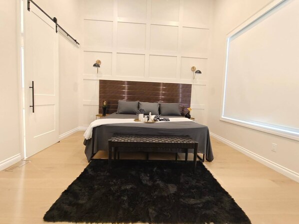 A bedroom with a bed, bedside lamps, a bench, and a large window. - Luxury Home With Three Bedrooms and Living Room (Calgary)