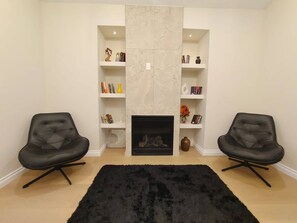 Ein Wohnzimmer mit zwei schwarzen Sesseln, einem Kamin und weißen Regalelementen.