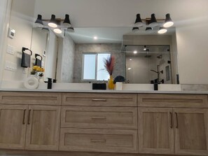 A bathroom with a large mirror, wooden cabinets, and a window. - Luxury Home With Three Bedrooms and Living Room (Calgary)