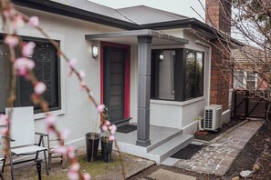 Ein Wohnhaus mit überdachter Veranda, einer roten Tür und einem Backsteinsschornstein.