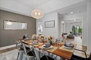 A dining area with a long table set for six, a chandelier, a mirror, and a framed quote on the wall.