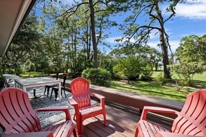A deck with red Adirondack chairs, a white table, and a view of a well-maintained lawn and trees.